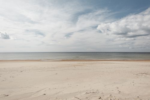 Free Scenery view of sandy shore against endless ocean under sky with fluffy clouds in daylight Stock Photo