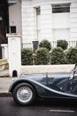 Fragment of old timer black automobile parked on asphalt road near white residential building with fence on street in town