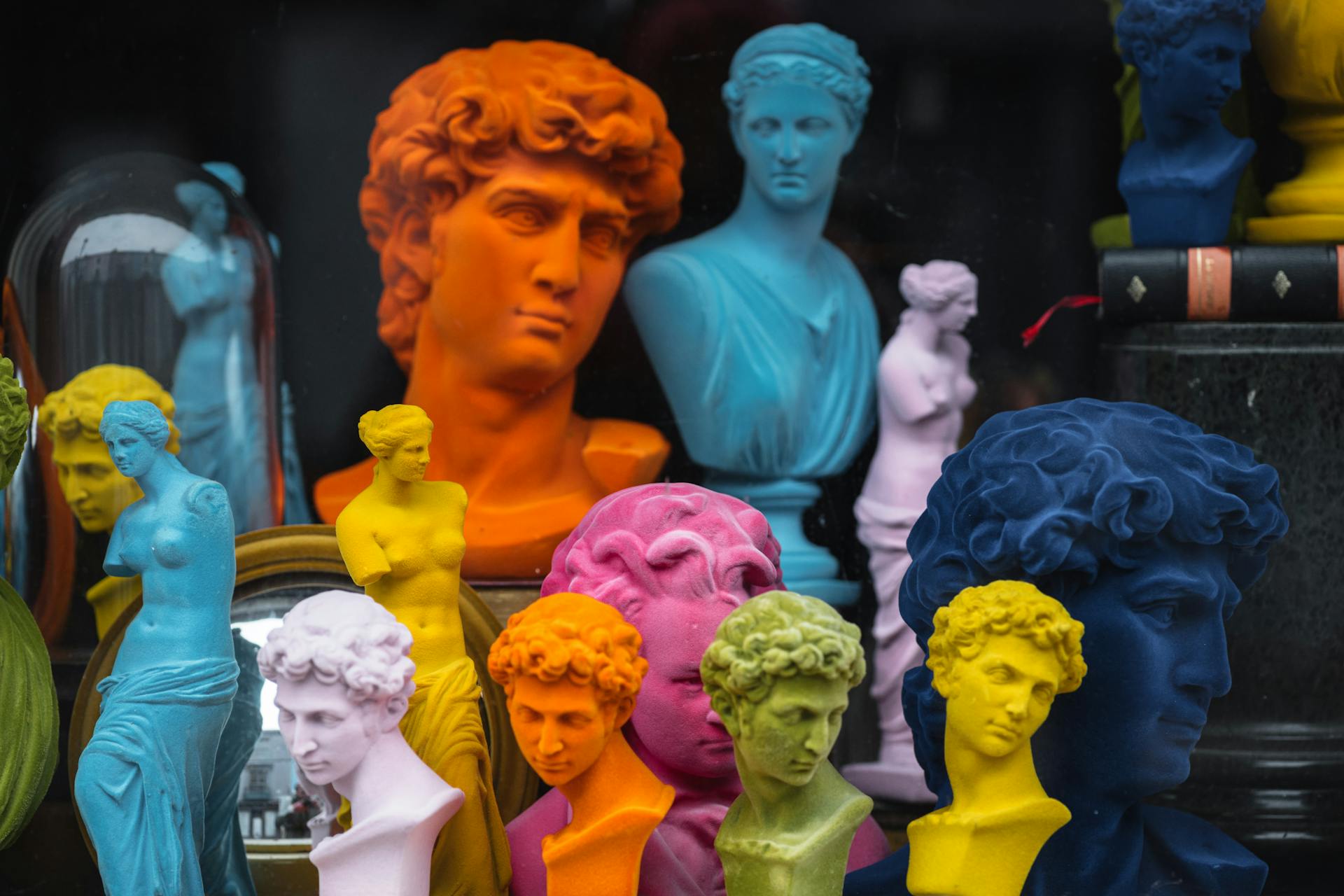 Multicolored head sculptures of David near bright statuettes placed in store with abundance of souvenirs and black pillar with book