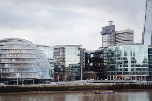 Contemporary buildings with glass walls located on street in financial district on embankment near calm Thames river in modern city