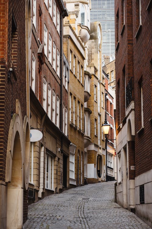 Narrow empty paved alley between aged stone residential houses with many windows and arched passage located on street of town