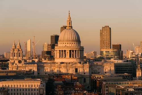 Aged famous cathedral with dome framed by the spires of churches located near buildings against modern skyscrapers on streets of London