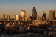 Contemporary multistory buildings and residential houses located near Thames river and suspension bridge in London city against cloudless sky in sunlight