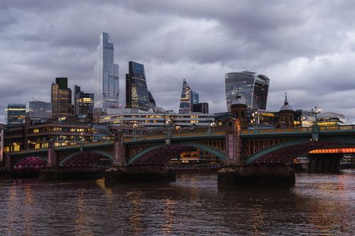 Free Bridge with glowing lights crossing calm Thames river located against contemporary famous multistory office buildings in London on evening time Stock Photo
