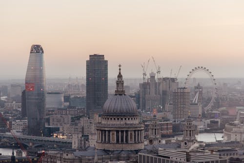 Free Cityscape of London with historic St Pauls cathedral with dome located near modern multistory skyscrapers and famous observation wheel near river Stock Photo