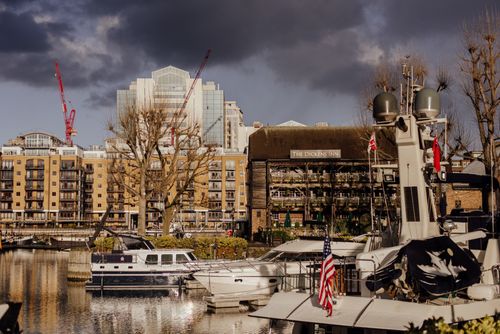 Free Modern vessels floating near pier with flag on calm river Thames near residential buildings and famous pub in London against cloudy sky Stock Photo