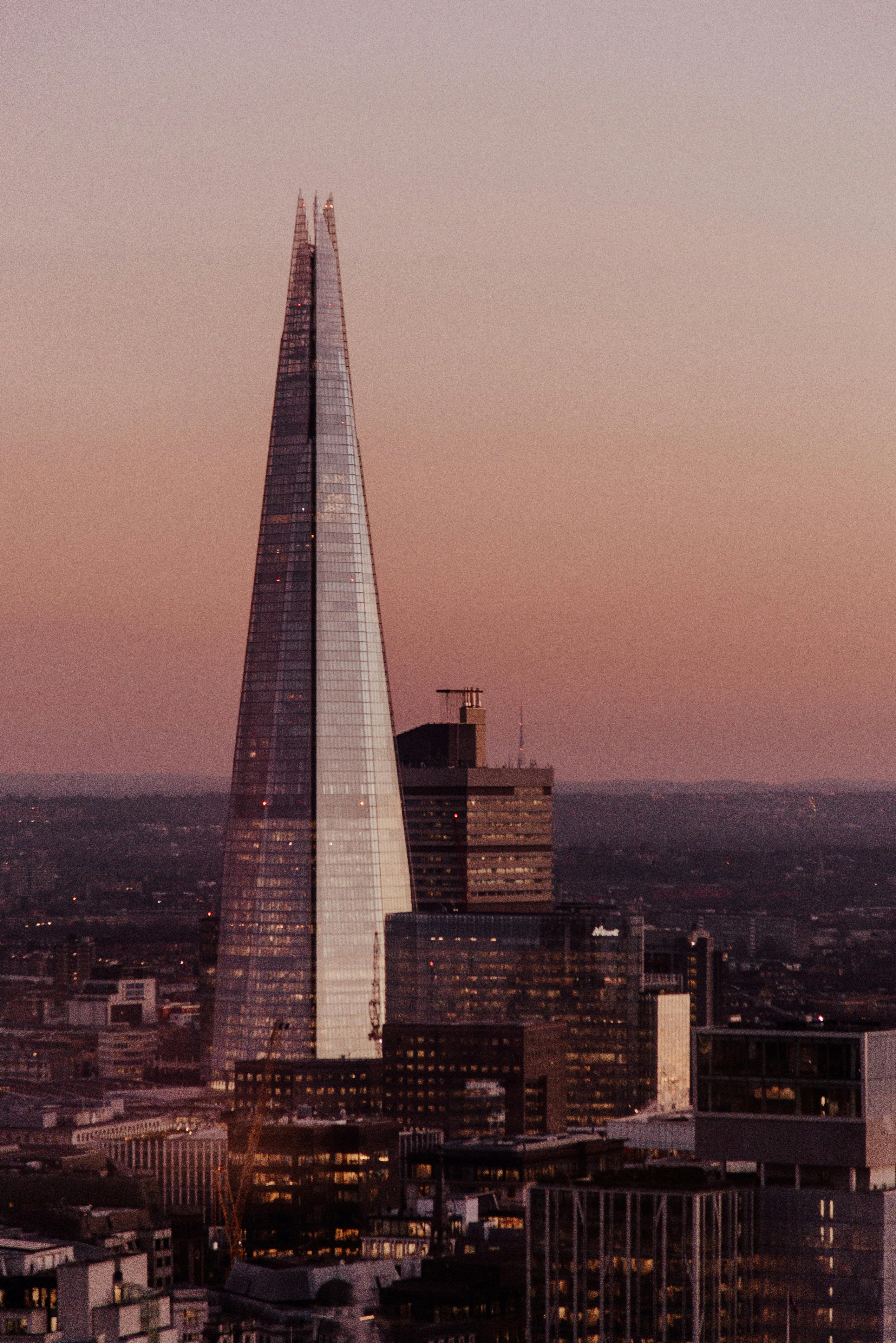 pyramid shaped glass skyscraper and modern multistory building under sundown sky in city