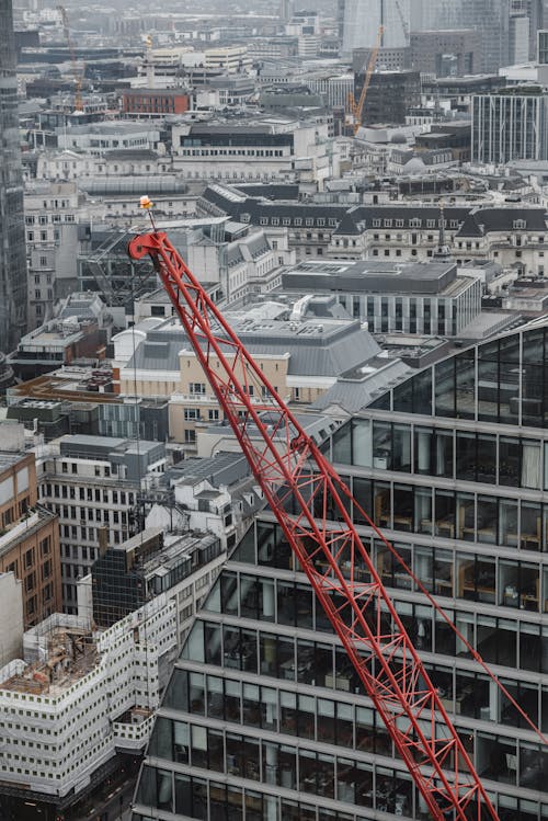Aerial view of red tower crane between multistory buildings and glass skyscrapers on cloudy day in London