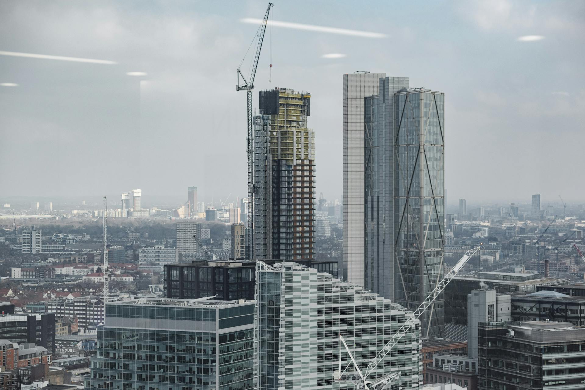 Complex of modern multistory buildings and commercial skyscrapers with tower cranes under cloudy sky in London