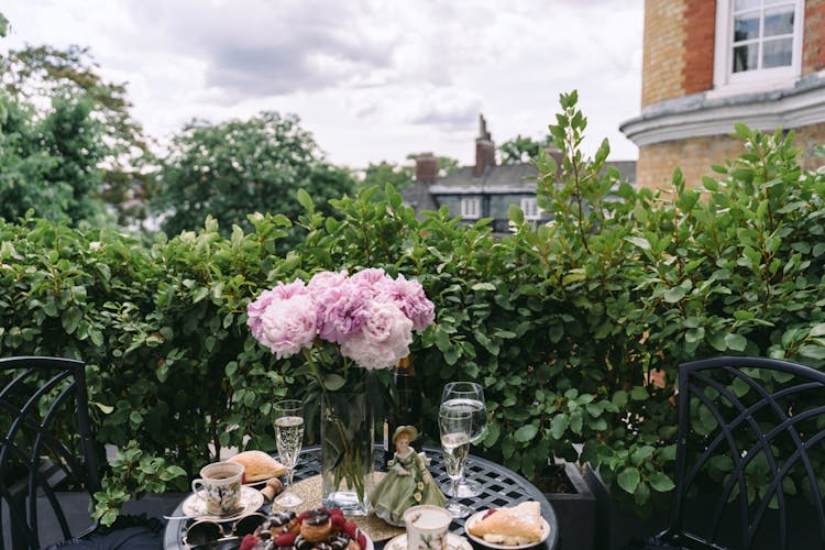 Round Table With Flowers Bouquet Arranged With Wineglasses And Coffee Cups In Garden