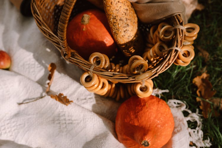 Red Kuri Squashes With Bread In Wicker Basket Placed On Blanket On Lawn In Sunlight