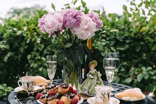 Free Breakfast table with profiteroles and champagne glasses decorated with flowers bouquet and figurine in garden Stock Photo