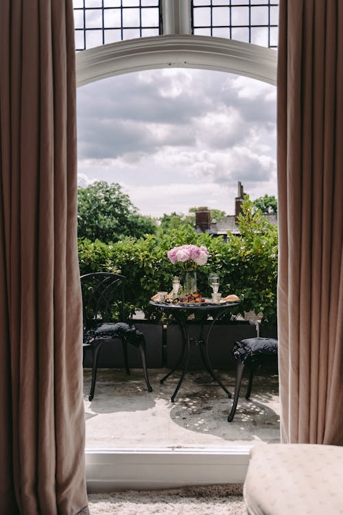 Veranda of classic styled villa with chair and round table served with food and drinks and decorated with bouquet of fresh peonies on sunny day