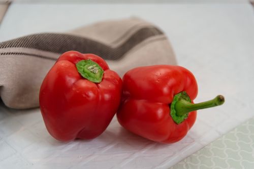 Free Whole ripe red bell peppers with green peduncles placed on table with tablecloth near rolled brown napkin in light room Stock Photo