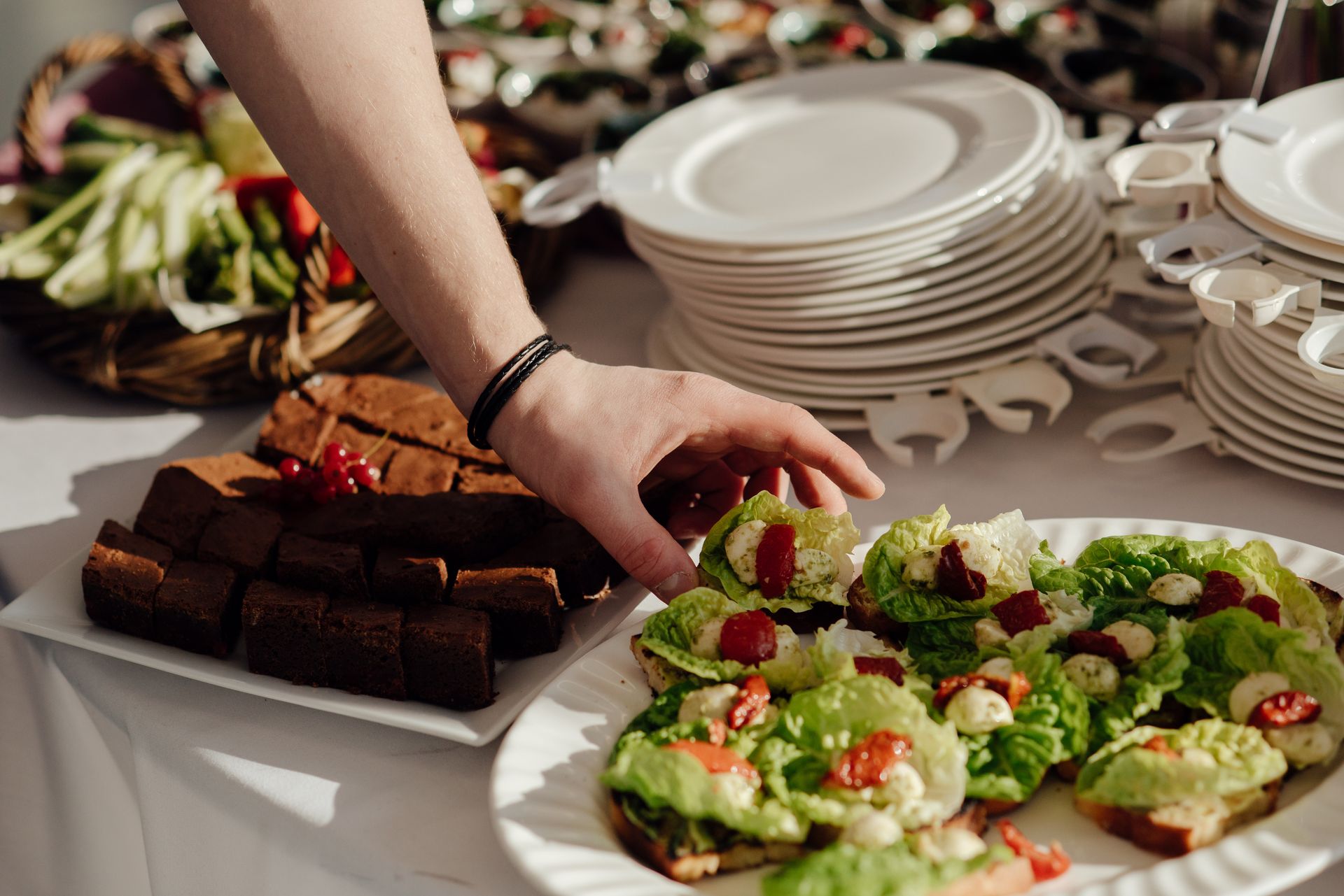 Crop anonymous man taking snack with lettuce and cherry tomatoes with cheese from buffet table with brownie during banquet in restaurant