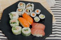 From above of black table with various rolls and sushi with fresh salmon placed on table with rolling bamboo mat