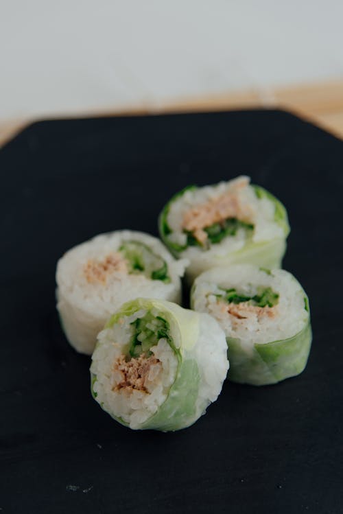 Free Tasty sushi rolls with rice and fish covered with green cabbage served on black plate on table in light room Stock Photo