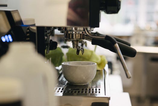 White mug placed on cup holder of modern coffee maker in contemporary light cafeteria with professional equipment on blurred background