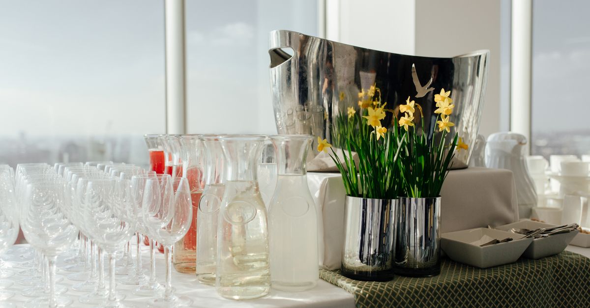Wineglasses near glass bottles of refreshment drinks placed in table near yellow flowers in light room near window during banquet
