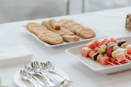 Free Tasty cookies placed near plate with skewers of fresh watermelon plums and grapes served on table with cutlery in cafe Stock Photo