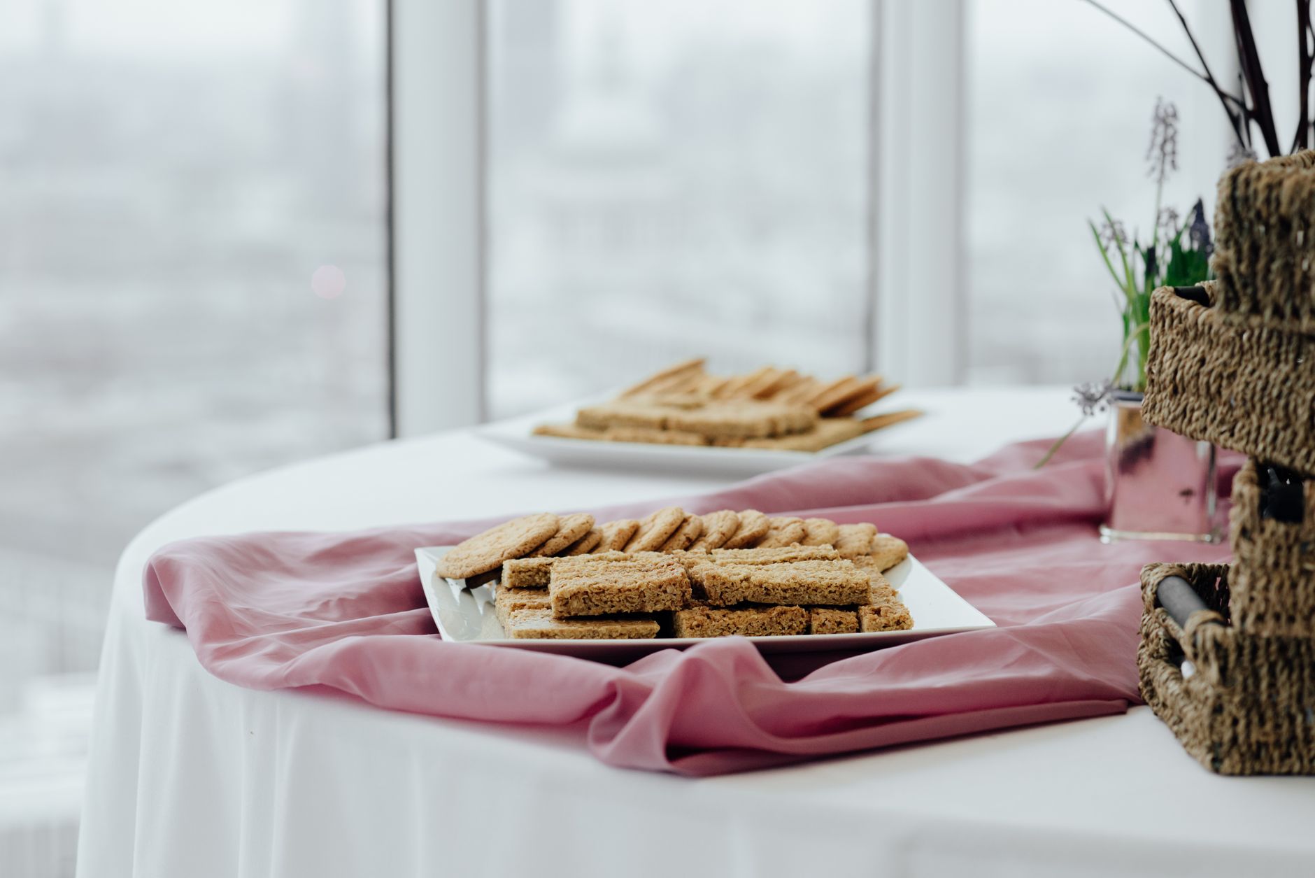 Delicious breakfast served in square shaped plates on pink fabric on blurred background of window