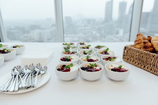 From above of continental breakfast with bowls of yogurt and granola placed in rows near plate with metal shiny clean spoons