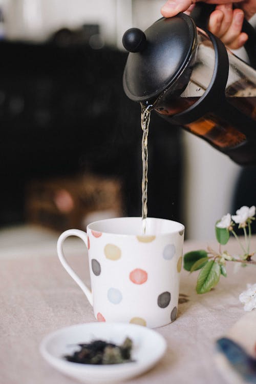 Crop anonymous person pouring delicious fragrant tea into mug on table on blurred background