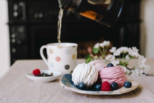 Cup filling with hot tea near plate with delicate zephyrs
