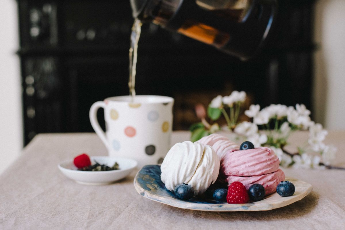 Delicious sweet zephyrs with fresh blueberry and raspberry on plate near mug filling with fragrant tea