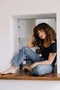 Woman in Black Tank Top and Blue Denim Jeans Sitting on Brown Wooden Seat