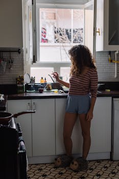 Woman standing in a kitchen, enjoying a quiet moment by the window.