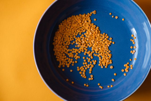 Dry red lentils scattered across a deep blue plate on a bright yellow background