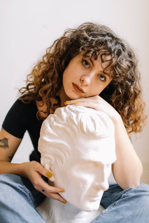 Woman in Black T-shirt and Blue Denim Jeans Holding a Head Bust