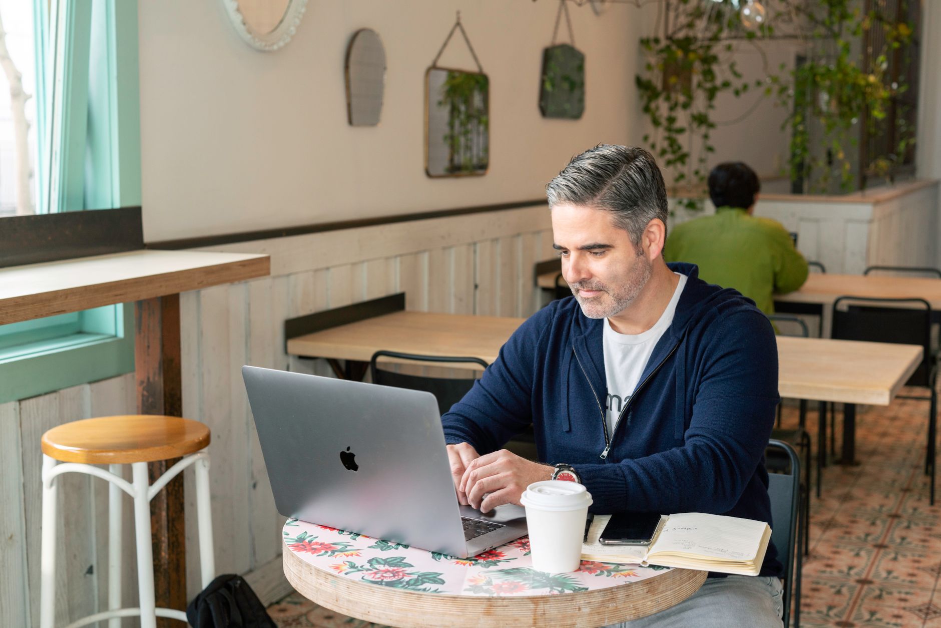 Adult man using a laptop for remote work in a cozy coffee shop setting with natural lighting.
