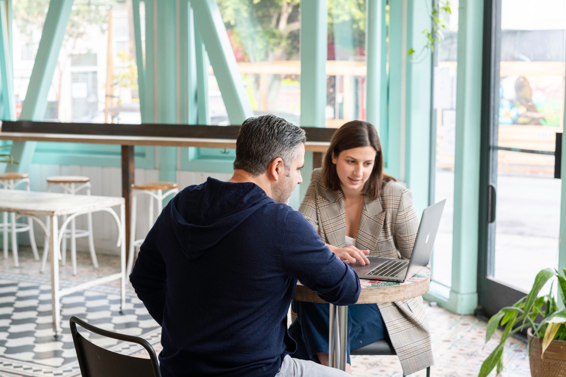 Two professionals collaborating over laptops in a cafe meeting setting.