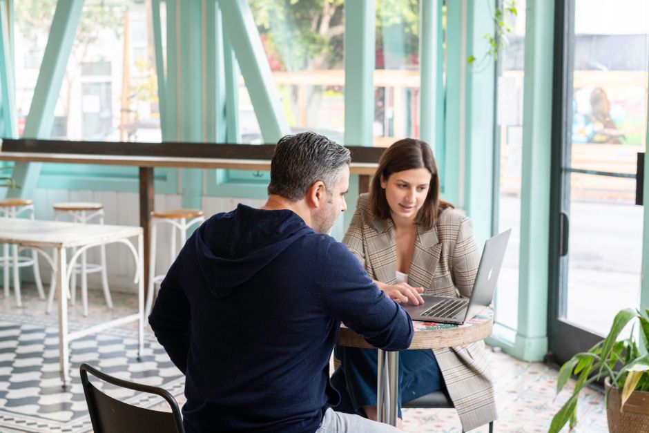 Two people talking over a laptop in a coffee shop
