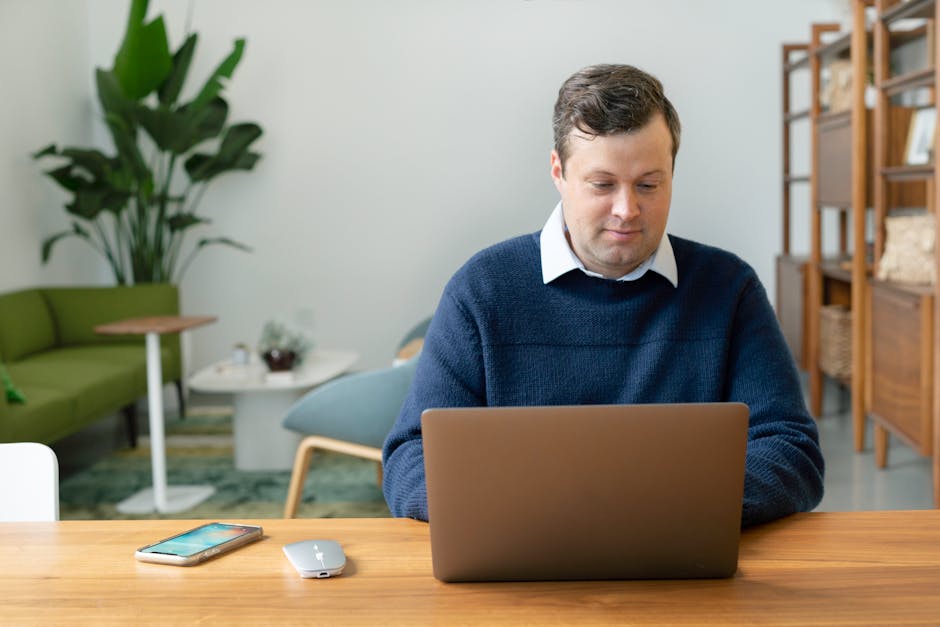 Does SoFi Actually Help Build an Emergency Fund? Caucasian man using a laptop in a modern living room setting with plants and shelves.