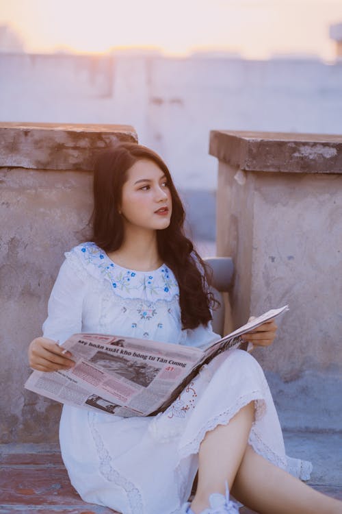 Free A Woman in White Dress Reading Newspaper Stock Photo