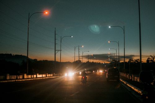 Free A scenic road at twilight with illuminated street lamps and passing vehicles, creating a serene evening ambiance. Stock Photo