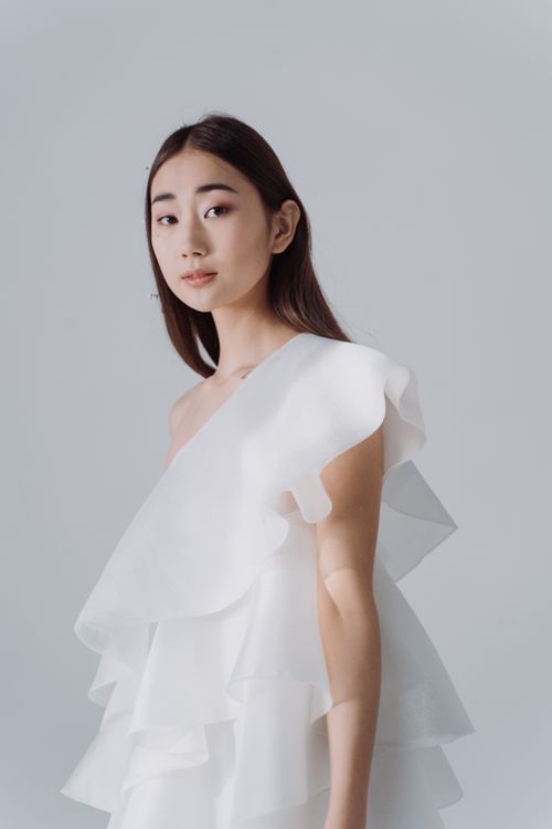 Free Elegant portrait of a woman in a flowing white dress with a minimalist white background. Stock Photo