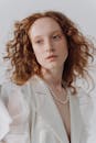 一位红发女子的肖像，她穿着白色衬衫，留着卷发，白色背景上戴着珍珠项链
