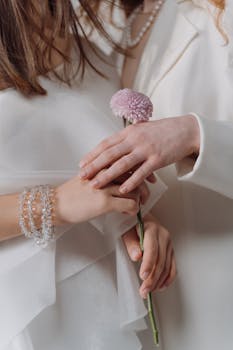 Close-up of two people holding a pink flower, showcasing elegance and gentle touch.