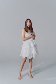 Beautiful Asian woman posing elegantly in a white dress against a studio backdrop.