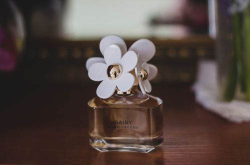 Free Close-up of a Marc Jacobs Daisy perfume bottle with flower caps on a wooden table. Stock Photo