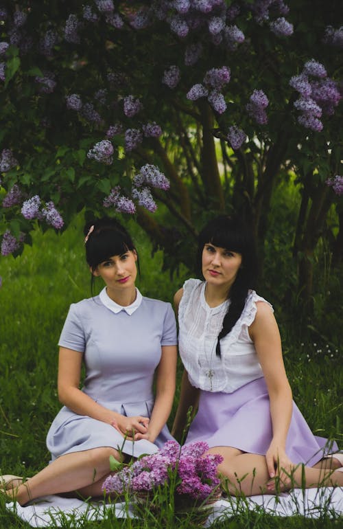Free Two Women Wearing Purple Dress Sitting Side-by-side on Grass Field Stock Photo