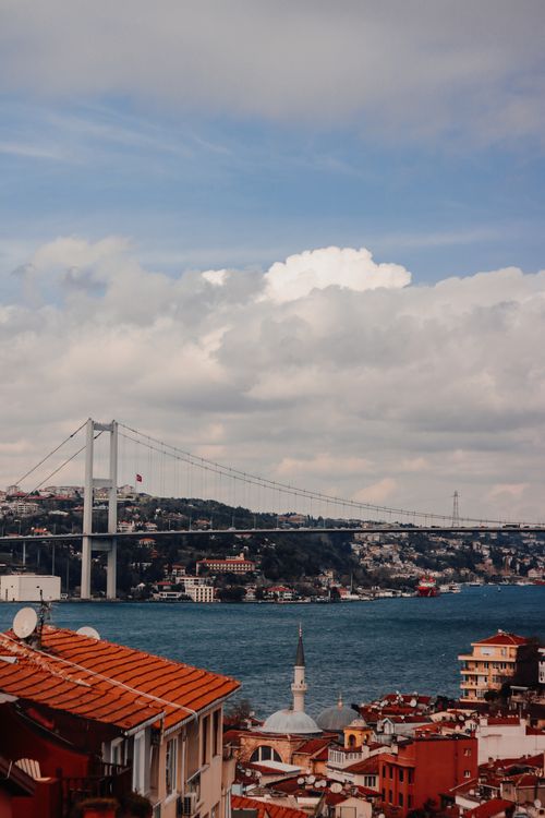 Free Scenic cityscape of Istanbul featuring the iconic Bosphorus Bridge and waterfront buildings under a partly cloudy sky. Stock Photo