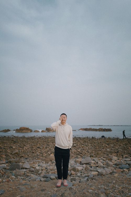 Free A man in a white hoodie poses on a rocky seashore, showcasing casual fashion by the sea. Stock Photo