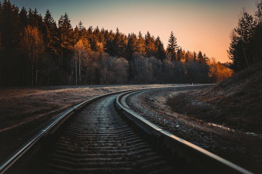 A serene view of a railway track in a forest at sunset with Autumn colors.