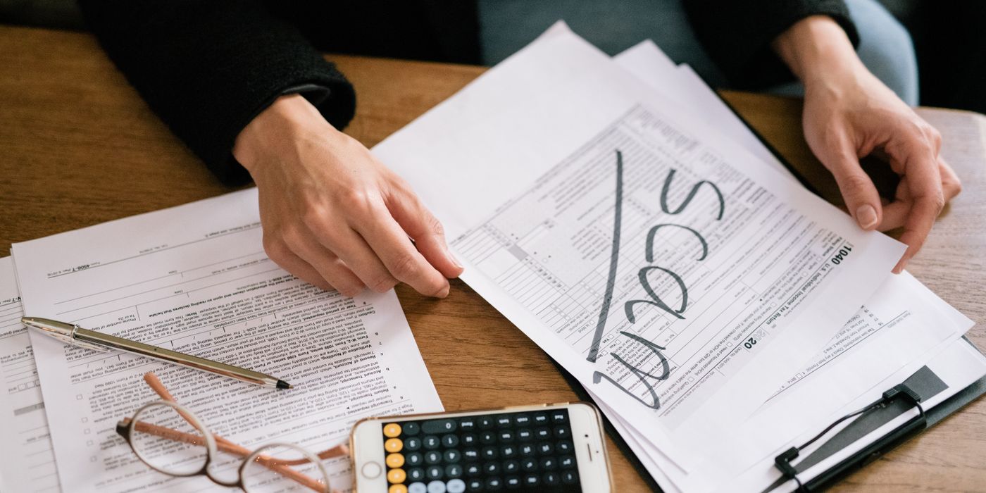 Hands of a person examining tax forms labeled as scam with calculator and papers.