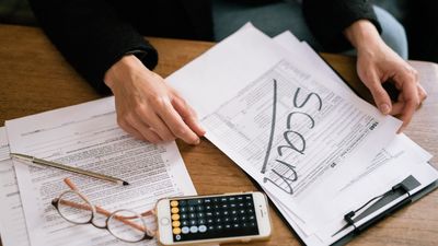 Documentos tributarios con la palabra Scam tachada, junto a un celular con calculadora, sobre impuesto a la herencia Chile